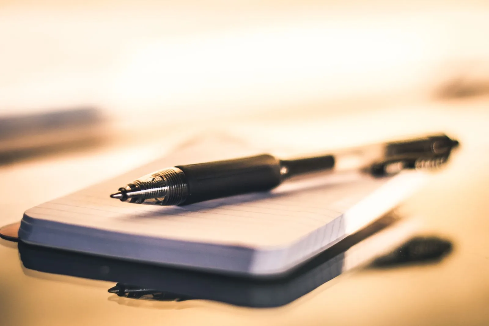 Black ballpoint pen resting on an open lined notebook in warm light