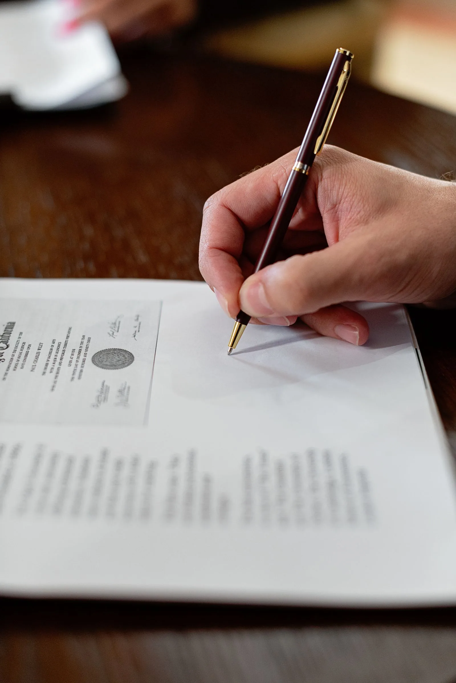 Close-up of a hand signing a printed document with a pen, illustrating pens for check writing